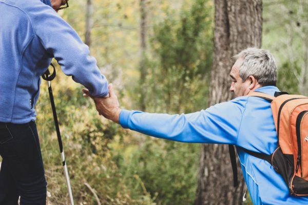 A man helps another man with a disability to hike through bushland